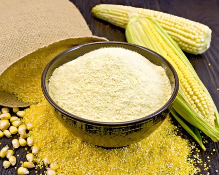 Flour corn in bowl with bag on board Flour corn in a bowl on the grits, cobs and grains, a bag on a wooden boards background