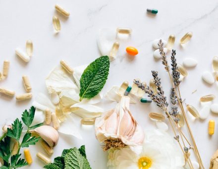 A flatlay of natural herbs, supplements, and flowers on a marble background.