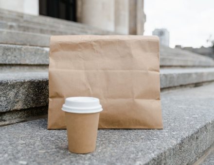 A paper bag with a coffee cup on stone steps in an urban outdoor setting.